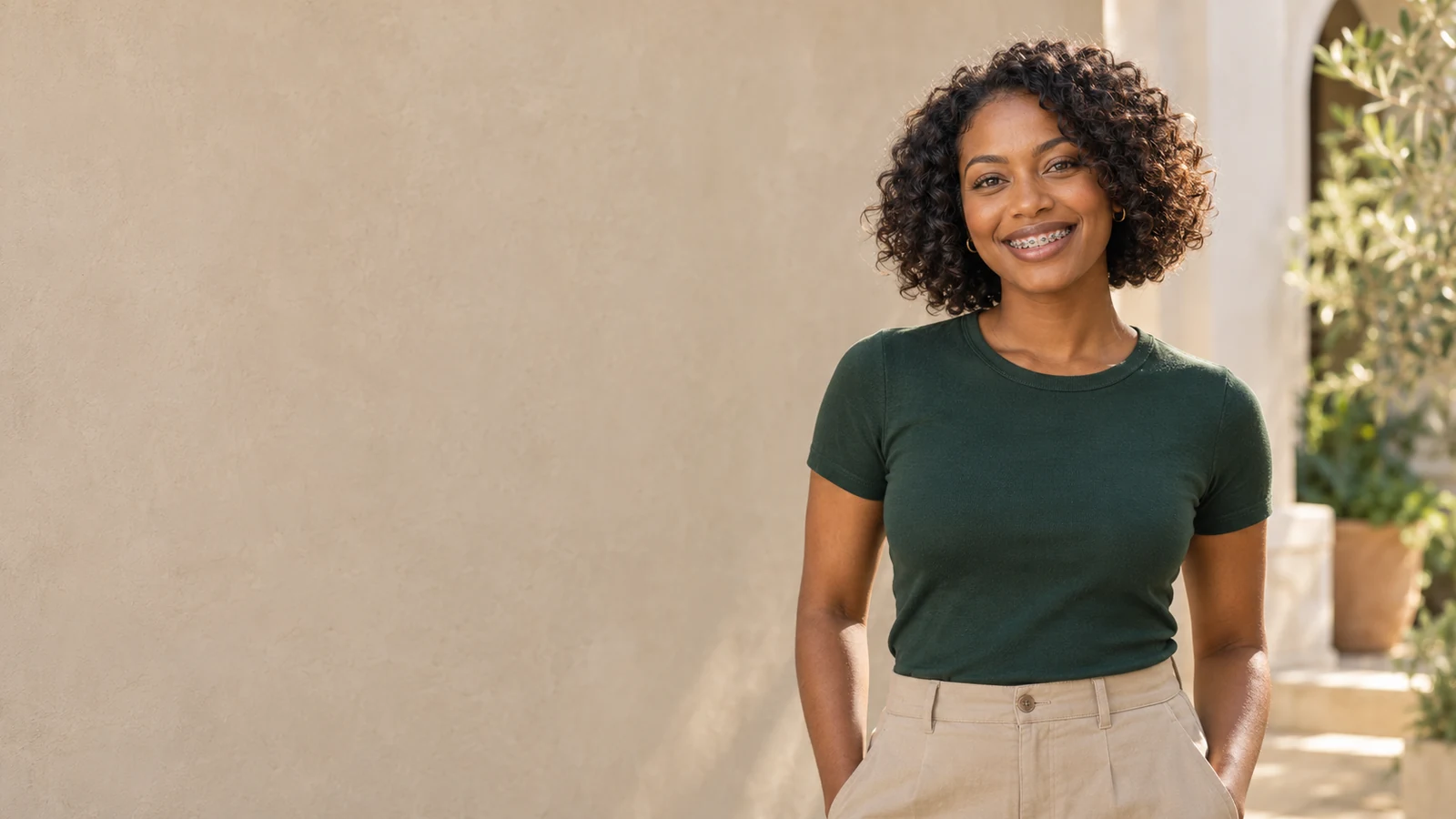 An adult woman smiling with metal braces in a sunlit courtyard.